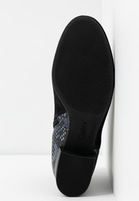 Semelle d'une bottine noire avec grip texturé, talon bloc, zip latéral et motif peau de serpent sur le talon et le panneau latéral.