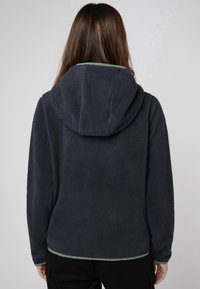 Donkerblauwe fleece hoodie met een zachte textuur, voorzien van een grote capuchon en groene accenten aan de onderrand en mouwen. Eenvoudig, casual ontwerp.