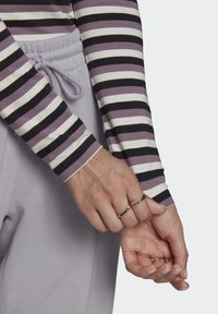 Prúžkované dlhé rukávy v purpurovej, čiernej a bielej farbe v kombinácii so šedými nohavicami s elastickým pásom. Strieborné prstene na prstoch, ktoré zvýrazňujú outfit.