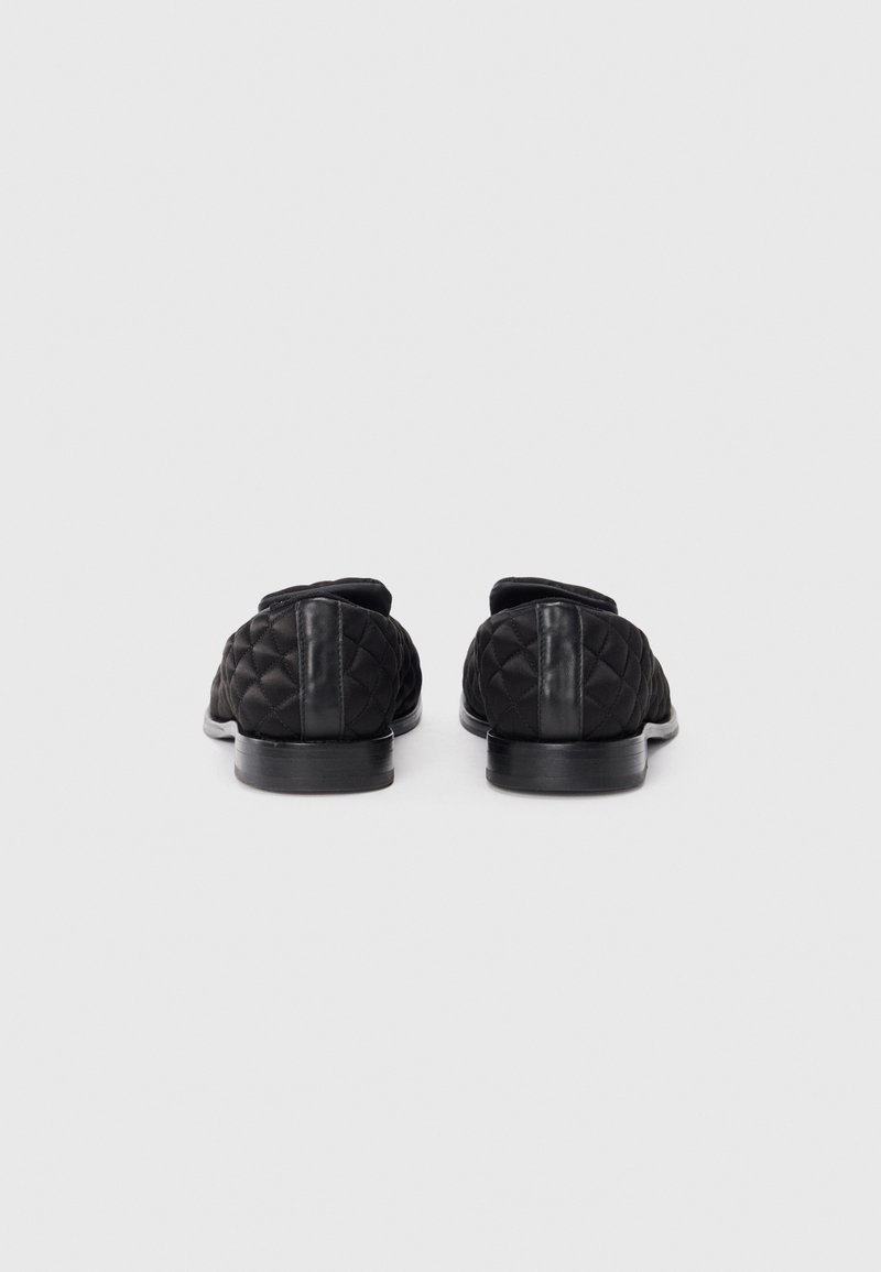 Zwarte gewatteerde schoenen van achteren, met een gladde zwarte leren accent op de hak en een lage, ronde zwarte rubberen zool.