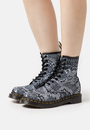 Bottes à lacets en cuir imprimé serpent noir et blanc avec une surface texturée, des coutures jaunes et une semelle épaisse noire. Soutien renforcé de la cheville.