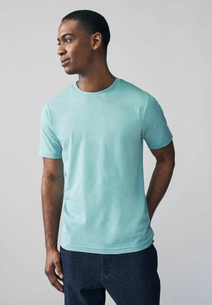 Camiseta de manga corta en color verde menta hecha de algodón suave, con cuello redondo y un corte relajado, combinada con jeans de denim oscuro.