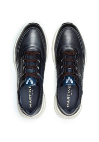 Laivastonsiniset nahkakengät ruskeilla nauhoilla, joissa on teksturoitu muotoilu sivuilla ja valkoinen kumipohja. Brändin nimi näkyy sisällä.