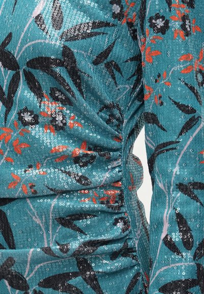 Teal pailletestof med blomsterdesign i sort og orange, med sammensyninger på siden, der skaber struktur og dimension.