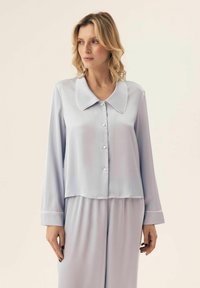 Jasnoniebieski satynowy zestaw piżamowy składający się z koszuli z kołnierzykiem, zapinanej na guziki, z długimi rękawami oraz dopasowanych spodni o miękkiej fakturze z białymi lamówkami.