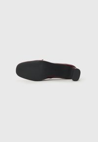 Burgunderfarget lærhøyhelet sko med en teksturert svart gummisåle og minimalistisk design, med rund tå og liten hæl.