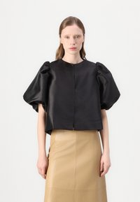 Schwarzes Satin-Cropped-Top mit puffärmel und Rundhalsausschnitt, kombiniert mit einem beigefarbenen Lederrock mit sichtbaren Nähten und gerader Silhouette.