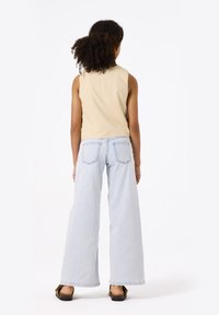 Top sin mangas color beige combinado con jeans de pierna ancha en azul claro. Los jeans cuentan con un diseño clásico de cinco bolsillos y un corte relajado.