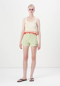 Lysegrønne denimshorts med frontlommer, med en lilla logo-lap. Kombinert med en kremfarget ribbet tanktop med rødt og oransje bånd.