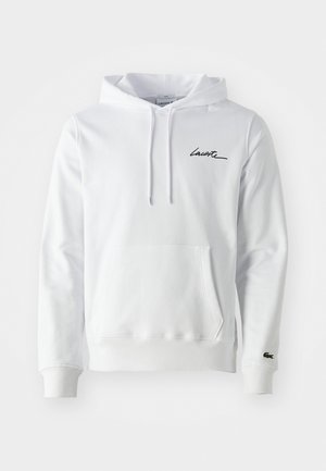 Bela kapuca s puloverjem z sprednjim žepom, črn napis "Lacoste" na prsih in majhen zeleni krokodilov logotip na levem manšetu.