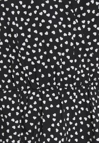 Tissu noir avec petits motifs de cœurs blancs. Ceinture froncée avec plis, texture douce, et motifs répartis de manière homogène sur toute la surface.