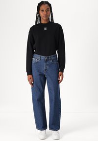 Sudadera negra con el logo "HUGO", combinada con vaqueros de denim azul de pierna recta y zapatillas blancas. Tejido suave y corte relajado.
