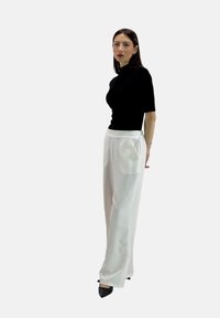 Top corto nero a maniche corte, aderente, abbinato a pantaloni bianchi a vita alta, larghi, con tasche laterali. Il modello indossa tacchi neri a punta.