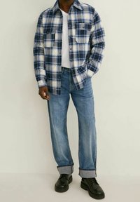 Rutigt skjorta i marinblått, vitt och ljusblått; två bröstfickor; matchad med ljusblå denimjeans; svarta skor; strukturerad tyg.