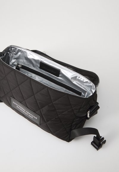 Schwarze, gesteppte Tasche mit silbernem Innenfutter, versehen mit einem Logo-Patch auf der Vorderseite und einer Reißverschluss-Tasche. Inklusive verstellbarem Tragegurt und Hardwareakzenten.
