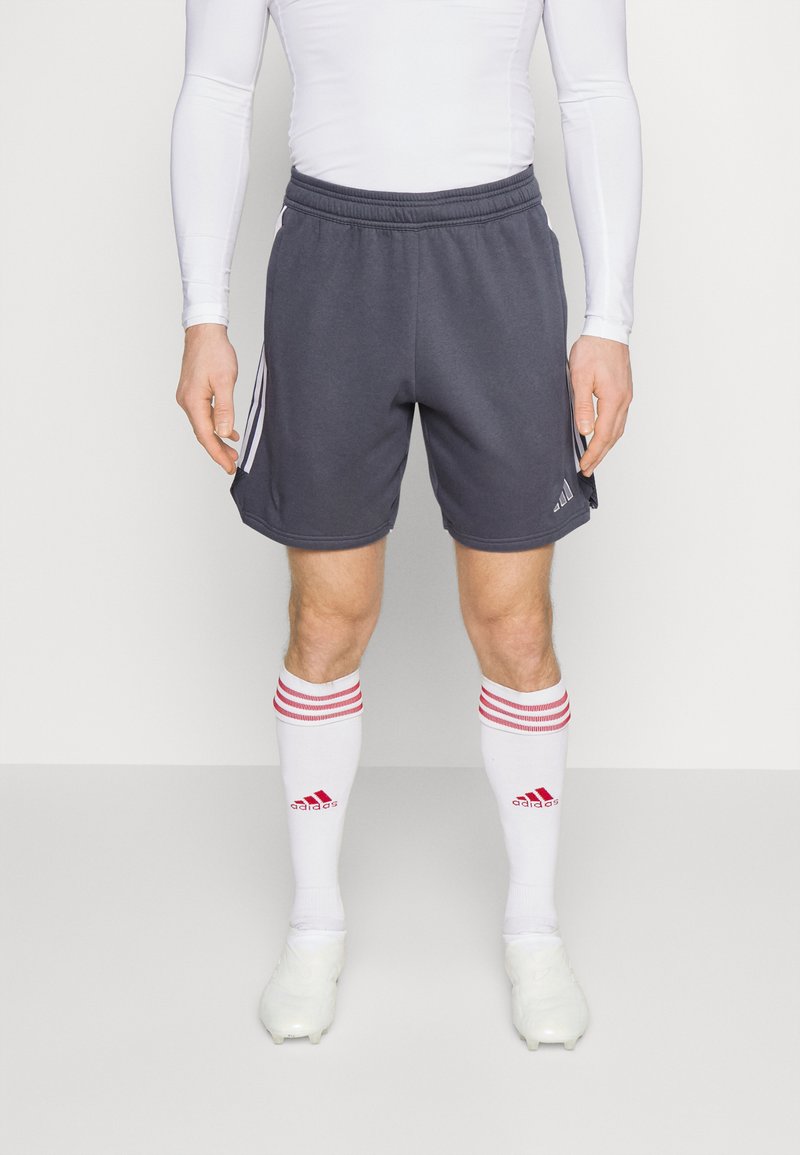 Graue Sportshorts mit elastischem Taillengummi und seitlichen Streifen. Getragen mit weißen Socken mit roten Streifen und weißen Fußballschuhen.