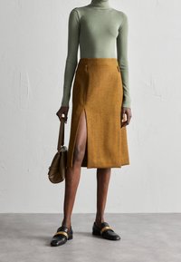 Brun herringbonekjol med en sidoklyv, i kombination med en ljusgrön polokrage. Till looken hör svarta loafers och en brun handväska.