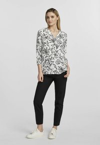 Biała bluzka z czarnym kwiatowym wzorem, dekolt w serek i rękawy do trzech czwartek, w połączeniu z czarnymi spodniami i białymi trampkami. Gładka tekstura materiału.