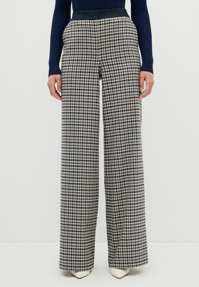 Kalhoty širokého střihu s houndstooth vzorem v námořnické modré a béžové barvě. Vyrobeno z tkané látky s hladkým povrchem a přiléhavým pasem.