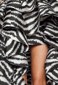 Svart och vit volangkjol med ett sicksackmönster. Tyget har en slät yta med en glansig finish och synliga sömdetaljer.