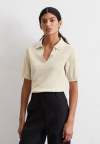Lichtbeige poloshirt met korte mouwen en V-hals, met een gestructureerd patroon. Gecombineerd met zwarte op maat gemaakte broeken voor contrast.