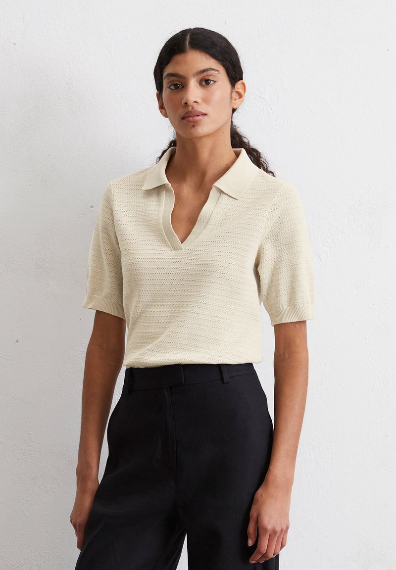 Lichtbeige poloshirt met korte mouwen en V-hals, met een gestructureerd patroon. Gecombineerd met zwarte op maat gemaakte broeken voor contrast.