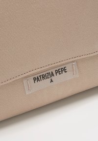 Beige textilní taška s texturovaným povrchem, na které je štítek s nápisem "PATRIZIA PEPE" v černé barvě na bílém pozadí.
