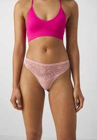 Roze crop top s tankićima u kombinaciji s roze tangama ukrašenim čipkastim detaljem, s složenim cvjetnim uzorkom i mekim tekstilom.