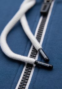 Niebiście niebieski materiał bluzy z kapturem z białym zamkiem i czarnymi zębami. Białe sznurki zakończone czarnymi plastikowymi końcówkami z napisem "Dimbre."