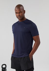 Maglietta sportiva blu navy con maniche corte, in tessuto traspirante, collarino tondo, abbinata a pantaloni corti neri. Nessun motivo o accento visibile.
