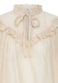 Blouse de couleur crème avec un col montant à volants, une ouverture en forme de goutte d'eau à l’avant nouée avec un nœud en tissu, et des détails volantés sur la poitrine et les épaules.