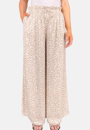 Beige, weit geschnittene Hose mit leichtem Leopardenprint und elastischem, gerafftem Bund, getragen mit weißem Oberteil und offenen Sandalen.