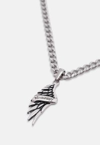 Ασημένιο κολιέ με αλυσίδα και μενταγιόν σε σχήμα φτερού με μαύρες λεπτομέρειες και την επιγραφή «Ed Hardy» στην περιοχή του φτερού.