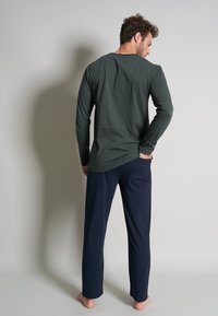 Olijfgroene blouse met lange mouwen, ronde halslijn, gecombineerd met marineblauwe broek, ontspannen pasvorm, zachte stof en zonder zichtbare patronen of accenten.