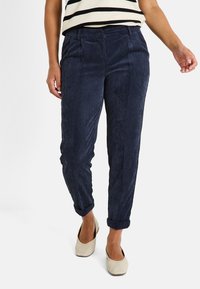 Pantalones de pana azul marino con textura de canales verticales, que cuentan con bolsillos frontales, un dobladillo con puños y una cinturilla con un solo botón.