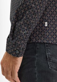 Camicia a fantasia scura con un design floreale nei toni del bordeaux, giallo e grigio. Due bottoni al polsino, realizzati in tessuto.