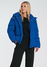 Niebieska puchowa kurtka z zapięciem na zamek i guziki, z odpinanym kapturem, dużymi przednimi kieszeniami oraz pikowanym wykończeniem dla ciepła.