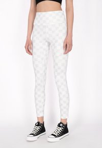 Lichtgrijze leggings met een geruit patroon, hoge taille en een stretchy materiaal, gecombineerd met zwarte hoog uitgesneden sneakers.