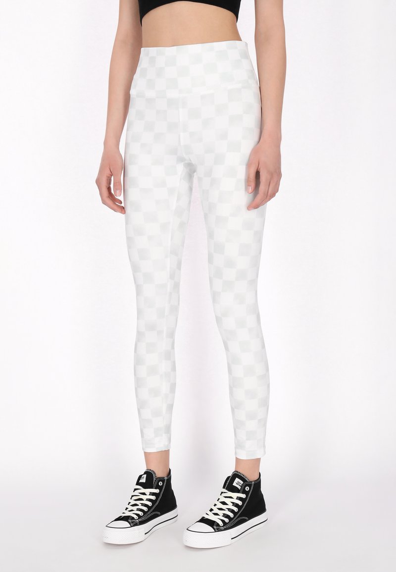Világosszürke leggings, kockás mintával, magasan záródó derékkal és rugalmas anyagból készült, fekete magas szárú tornacipővel párosítva.