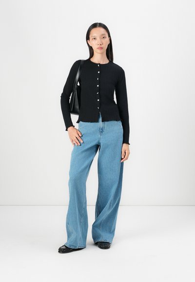 Black ribbed long-sleeve cardigan with round neckline and button closures, paired with wide-leg blue denim jeans and a black handbag.