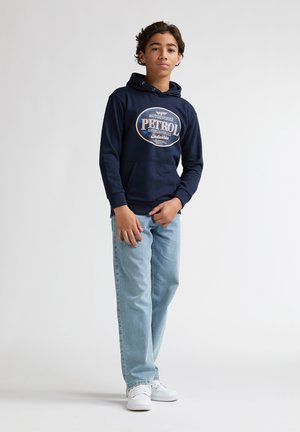 Hanorac bleumarin cu grafică "PETROL" pe față, asortat cu blugi albastru deschis și teniși albi. Materialul pare moale și casual.