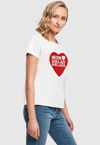 Tricou alb din bumbac cu un grafic roșu în formă de inimă, având textul „MEIN ♥ SCHLÄGT SCHLAGER.” Design cu mâneci scurte și croială lejeră.
