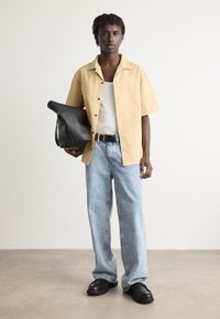 Short-sleeve yellow textured shirt, white tank top, light blue loose jeans, black belt, and black leather bag. Black lace-up shoes.
