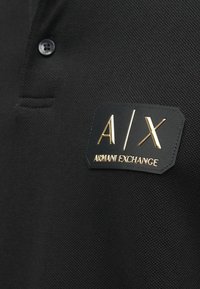 Melnā polo krekls ar teksturētu audumu, pogu aizdari un melnu birku ar zelta iepressētu "A/X" un "Armani Exchange".