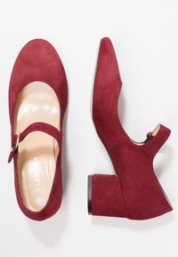 Des talons Mary Jane en cuir suédé rouge avec un bout rond, une bride de cheville et une boucle en métal, un talon bloc bas et une semelle intérieure en cuir lisse, présentés de dessus.