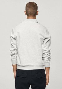 Vaaleanharmaa collegepaita, jossa on käännetty kaulus, resorit hihansuissa ja helmassa; pehmeä materiaali ja yksinkertainen muotoilu; yhdistetty tummiin housuihin, joissa on taskut.