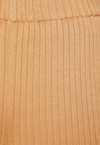 Ribbad stickad tyg i ljusbeige med vertikala ränder. Mjuk textur med ett midjeband upptill.