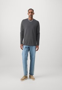 Cămașă gri cu mânecă lungă, blugi relaxați de culoare albastru deschis și pantofi slip-on bej. Design simplu, textură moale și culori neutre.