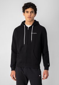 Sudadera negra con cremallera y cordones blancos, con el logotipo bordado de Champion en el lado izquierdo del pecho, que cuenta con un bolsillo frontal y puños acanalados.