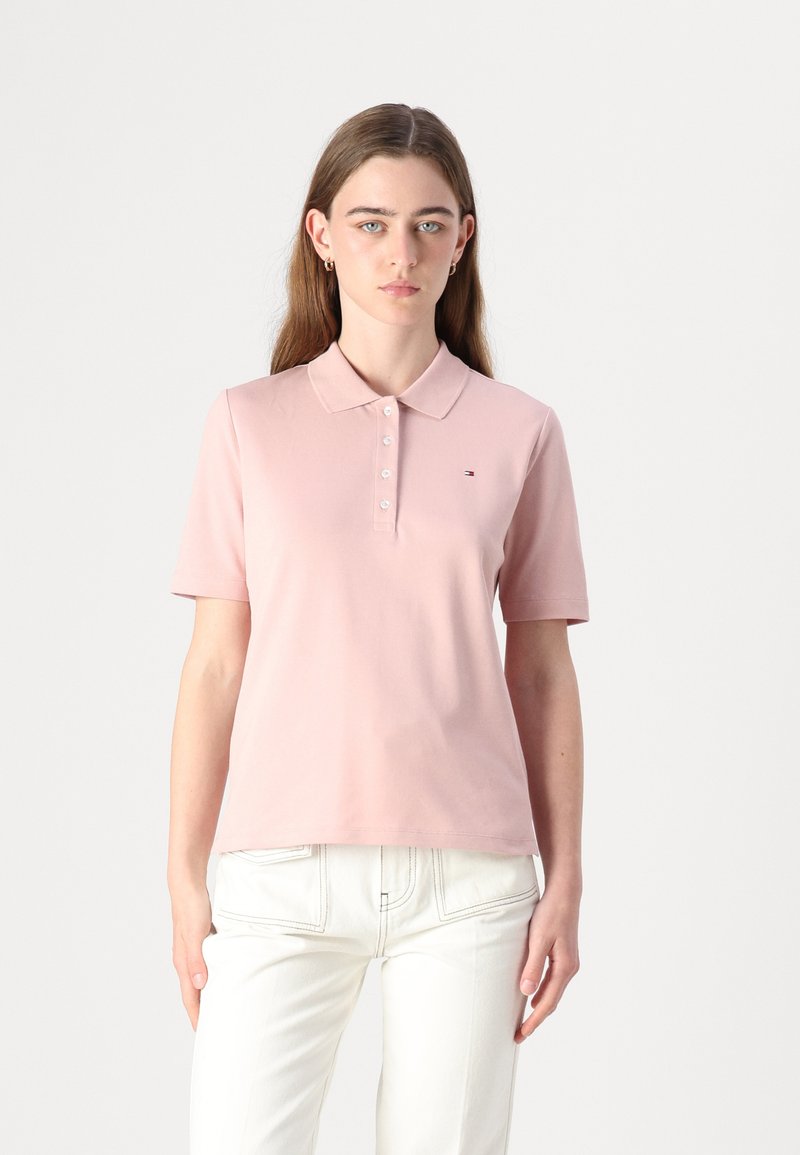 Polo de cor rosa claro, feito de tecido suave, com gola clássica e fecho de botões. Pequeno logo no lado esquerdo do peito.